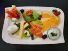 Gute-Laune-Frühstück mit Brotkorb (2 Brötchen, Körnerbrot, Baguette), Marmelade, Butter, Avocado, Lachs, Meerrettich, verschiedenen Käsesorten, Gemüsesticks mit Dip und gekochtem Ei – perfekt für einen genussvollen Start in den Tag bei Mokka & Minze.